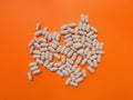 Pile of white pills on orange background. The upper angle of view. The concept of dietary supplements