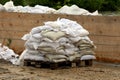 Pile of white sandbags used for flood protection put on wooden pallet waiting to be removed after flood surrounded with muddy