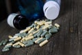 Pile of yellow and green capsules dispersed on wood table with tipped over pill boxes and blue empty bottle of alcohol Royalty Free Stock Photo