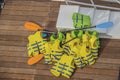 A pile of yellow and green life vests with boat paddles piled on a wooden dock and some white plastic stairs Royalty Free Stock Photo