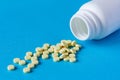 A pile of yellow tablets from a white plastic jar