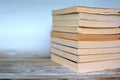 Pile of yellowed old used paperback books on wood desk and light blue background