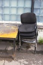 Piled old dirty dusty office chairs and a rusty weathered yellow metallic table standing outside