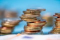 Piled up euro coins with blue background. Banknotes in front out of focus. European monetary union currency