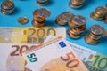 Piled up euro coins next to EUR banknotes. European monetary union currency. Cash on blue background, paper bills and piled up