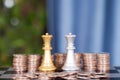Piles of dollar coins in front of the two queens of both chess players in a duel Royalty Free Stock Photo