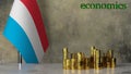Piles of gold coins on a marble table against the background of the flag of Luxembourg.