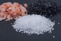 Piles of Hawaiian Black Lava Sea Salt, Coarse White Sea Salt and Himalayan Pink Salt on dark