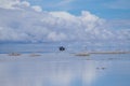 Piles of salt and an off-road vehicle in the background. The Salar de Uyuni flooded after the rains, Bolivia. Clouds reflected in Royalty Free Stock Photo