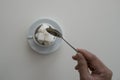 Piles of sugar cube in white cup with spoon and hand holding spoon.