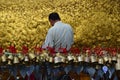 Pilgrim pasting gold foils onto golden rock at the Kyaiktiyo Pagoda, Myanmar with row of small bells in foreground