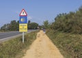 Pilgrims walking in the countryside and passing by a yellow shell sign that guides the pilgrims in the Camino de Santiago, Spain.