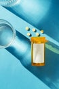 Pill bottle with blank label on blue background with yellow pills and a glass of water Royalty Free Stock Photo