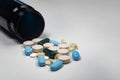 Pill bottle filled with assorted prescription tablets resting alongside a pile of vibrant pills