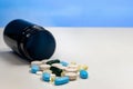 Pill bottle filled with assorted prescription tablets resting alongside a pile of vibrant pills