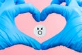 Pill with a screaming smiley inside a heart from hands in medical gloves on a pink background.Painkiller concept Royalty Free Stock Photo