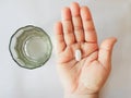 A pill on a woman`s palm and a glass of water in white background