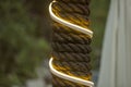 A pillar wrapped with thick rope. yellow white glowing garland with a rope against a background of blurred green wood and curtains Royalty Free Stock Photo