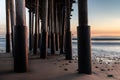 Pillars of Ventura Pier at sunset. Beach sand and rocks; smooth ocean and colored sky.