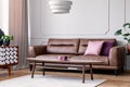 Pillows on leather couch in retro living room interior with lamp above wooden table. Real photo Royalty Free Stock Photo
