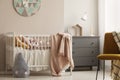 Pillows and toy in white wooden crib with pastel pink blanket in bright nursery