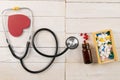 Pills in botle and wooden box with stethoscope and heart on white wooden table. Medical concept. Top views with clear space