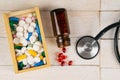 Pills in botle and wooden box with stethoscope and heart on white wooden table. Medical concept. Top views with clear space