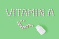 Pills dropped in shape of words vitamin A from bottle on green background. Flat lay, top view.