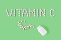 Pills dropped in shape of words vitamin C from bottle on green background.