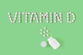Pills dropped in shape of words vitamin D from bottle on green background. Flat lay, top view. Health care and medical concept