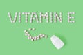 Pills dropped in shape of words vitamin E from bottle on green background. Flat lay, top view. Health care and medical concept