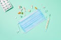 Pills, drugs, vitamins, clinical manual thermometer, blue surgical mask on pastel light green background.Colorful layout