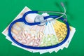 Pills, euros and stethoscope on green background