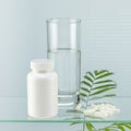 Pills and glass of water on glass shelf with palm leaves