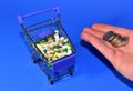 Pills and hand with money on blue background. Coins for payment of medicines. Shopping cart with pills. Medicine tablets and