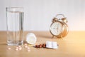 Pills,medicine bottle ,glass of water and clock on wooden table ,healthcare and medical concept