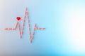 Pills in shape of cardiogram pulse on blue gradient background. Vitamins and red glass heart, symbol of healthy lifestyle.