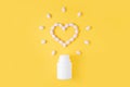 Pills in shape of heart dropped from bottle on yellow background. Flat lay, top view Royalty Free Stock Photo