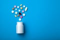 Pills spilling out of white plastic pill bottle on blue backgrou Royalty Free Stock Photo
