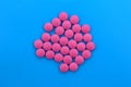 Pink pills lie in a pile on a blue background.