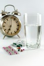 Pills with water in a clear glass and the alarm clock shows the time the medication is taken. Royalty Free Stock Photo