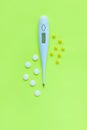 Pills and white digital thermometer on a yellow background. Flat lay, top view, minimalistic style. Royalty Free Stock Photo