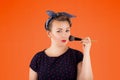 Pin-up woman portrait with bright colors and beautiful make-up in front of an orange background holding a make-up br in her hands. Royalty Free Stock Photo