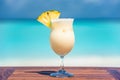 Pina colada coktail with slice of pineapple on wooden table at the beach