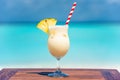 Pina colada coktail with straw and slice of pineapple on wooden table at the beach