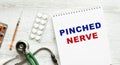 PINCHED NERVE is written in a notebook on a white table next to pills and a stethoscope