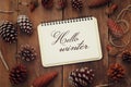 Pine cones and open notebook with text: HELLO WINTER