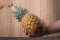 Pineapple being held Ripe pineapple being hold diagonally by a male caucasian hand with a wooden background.