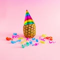 Pineapple with cap and colorul party streamers on pink background. Minimal party and celebration concept
