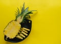 Pineapple cut in black ceramic bowl on yellow background. Copy space Royalty Free Stock Photo